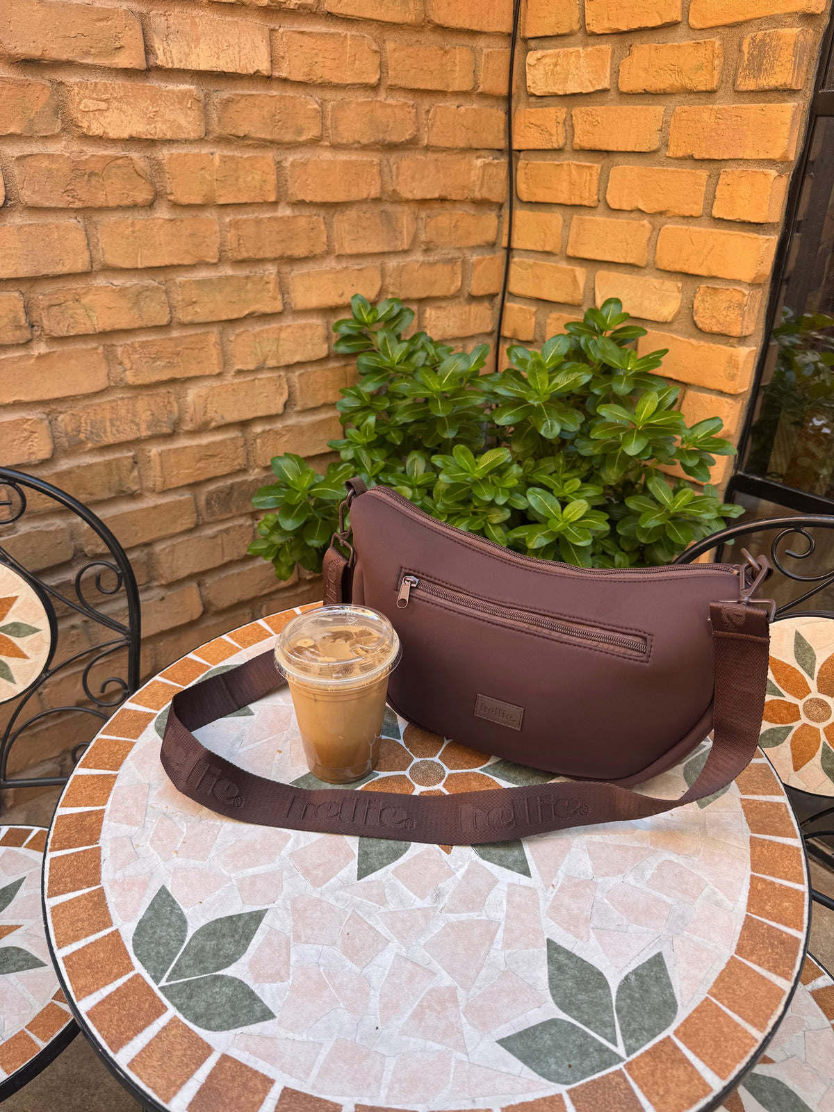 The espresso brown Bellie Crescent Bag on a mosaic café table